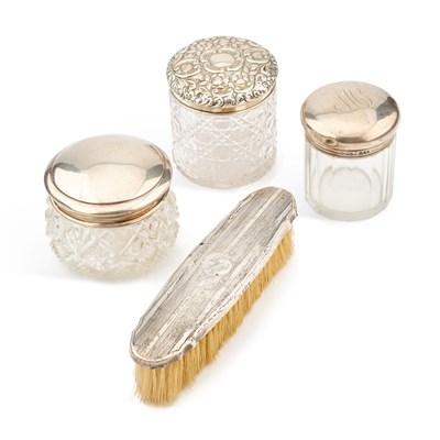 Lot 62 - THREE SILVER-TOPPED GLASS DRESSING TABLE JARS AND A SILVER-BACKED BRUSH